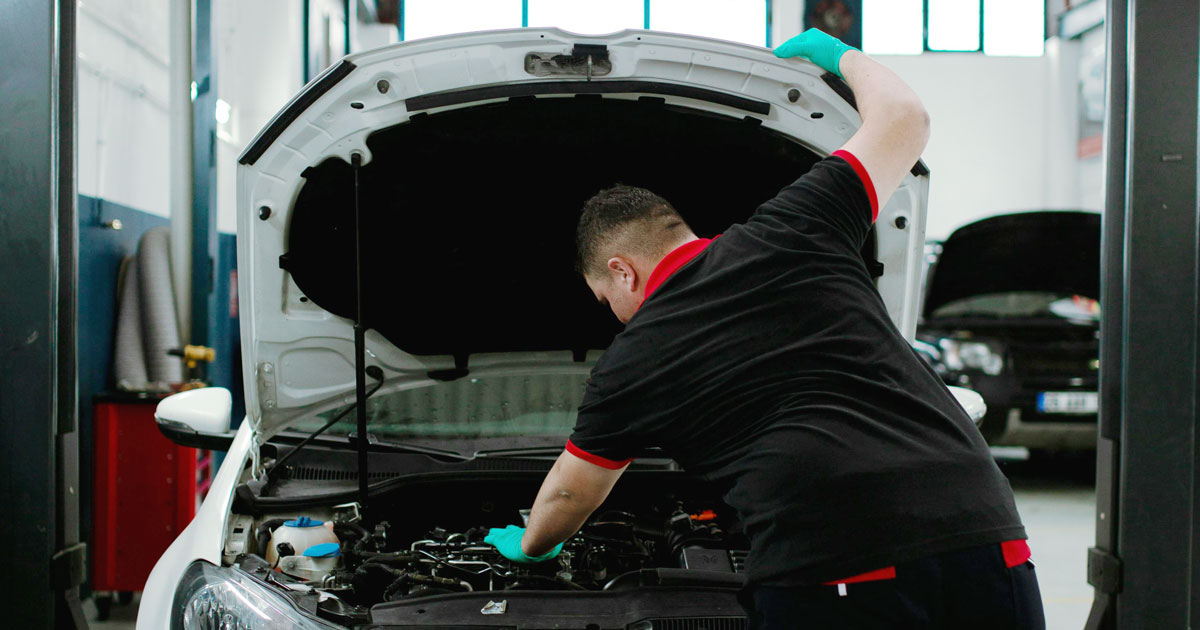 Henkilö tarkastamassa autoa konepellin alta.